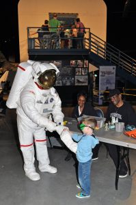 Child wearing goggles interacting with an astronaut in a full suit