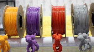 Spools of 3d printing filament in gold, purple, red, and gray, with small 3D printed balloon animals in front of each